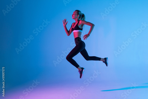 Sporty young woman fitness jumping isolated on purple light background