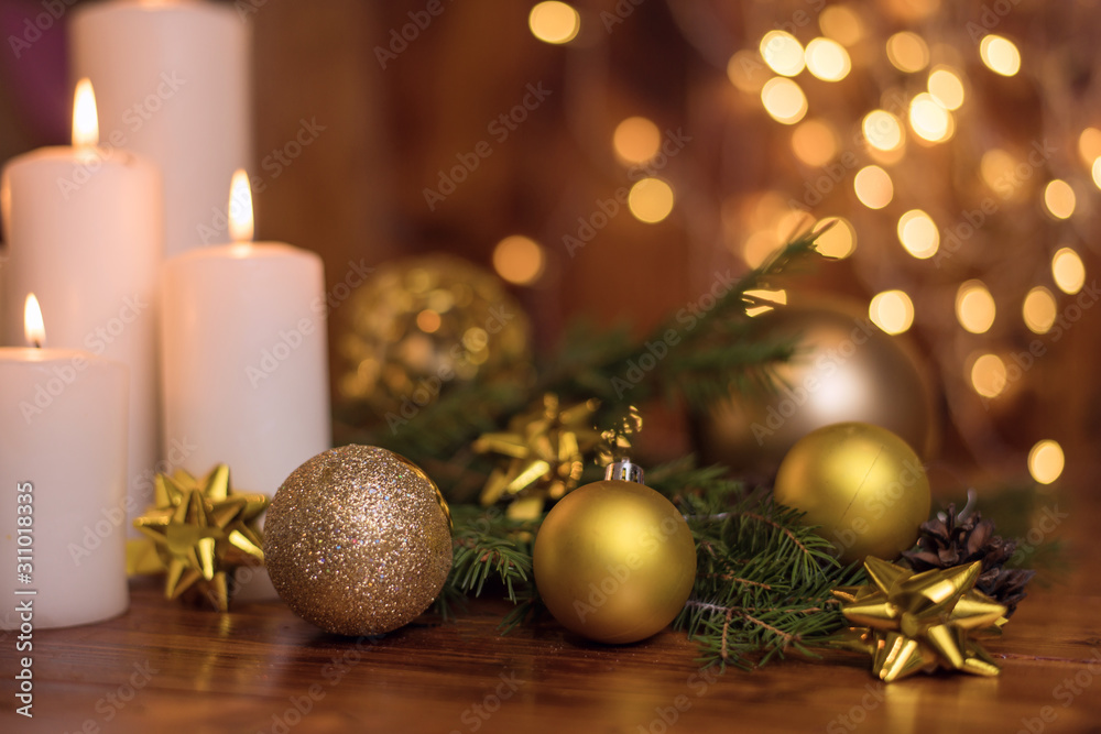 Golden Christmas ball on a tree branch, white candle flame with stars bokeh lights on a brown background 2020