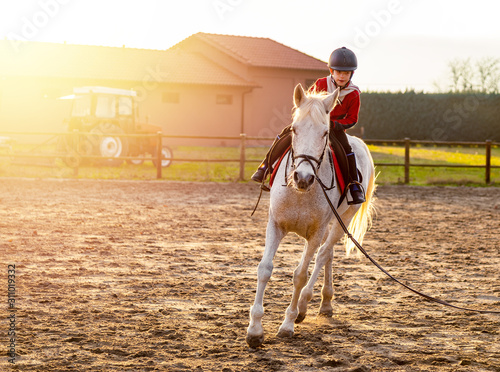 8 year boy riding white horse during sunset at ranch