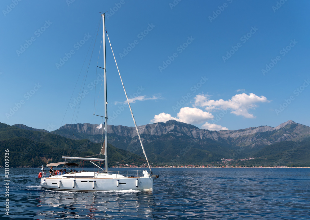 Sailing yacht in the sea against the backdrop of mountains at sunny day Sailing yacht in the sea against the backdrop of mountains at sunny day