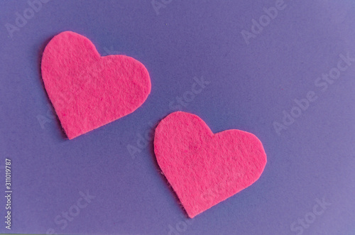 Pink felt hearts with green clothespins on a purple background. St. Valentine's Day and romance concept. Top view, flat lay. Copy space.