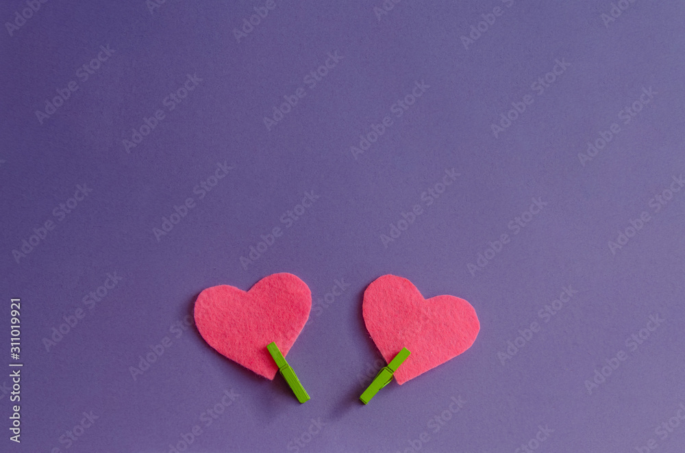Fototapeta premium Pink felt hearts with green clothespins on a purple background. St. Valentine's Day and romance concept. Top view, flat lay. Copy space.