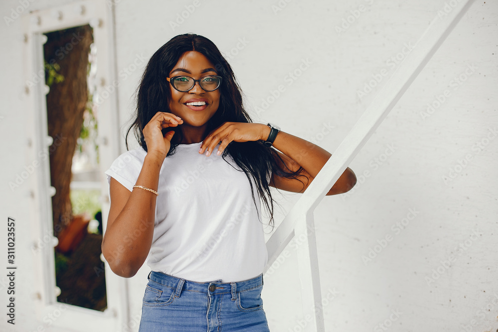 Cute black girl near white wall. Lady in a white t-shirt and blue jeans. Woman in a sunglasses. Cute black girl near white wall. Lady in a white t-shirt and blue jeans. Woman in a sunglasses.
