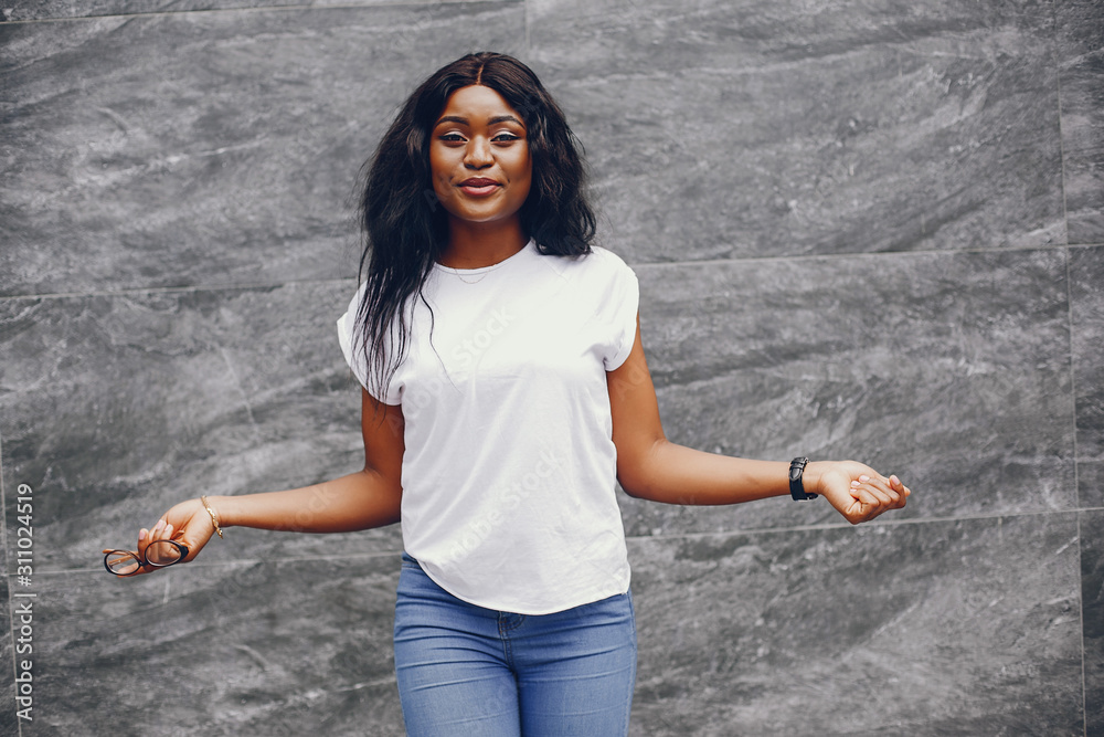 Se venligst Rejsende købmand enkel Cute black girl near gray wall. Lady in a white t-shirt and blue jeans.  Stock-foto | Adobe Stock
