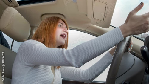 Pissed off displeased angry aggressive woman driving a car shouting at someone with hand fist up. photo