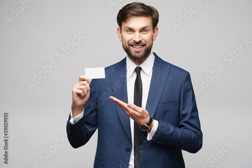 studio photo of young handsome businessman wearing suit holding business card