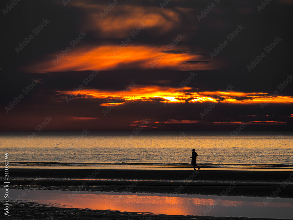 Fototapeta premium Single person running at an empty beach after colorful sunset in northern France