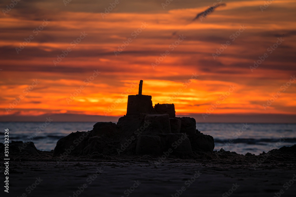 Sun setting in the ocean behind a silhouette of a sand castle at a beach in northern France