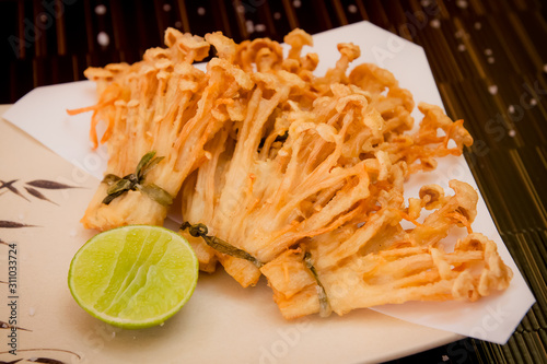 deep fried golden brown crispy Japanese enokitake needle shape mushroom with lime on black backgroundstock photo photo