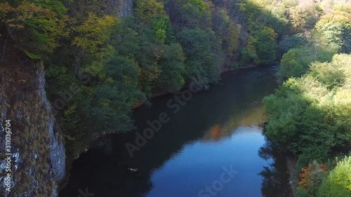 Forward drone shot of a river flowing through cliffs covered in autumn trees photo