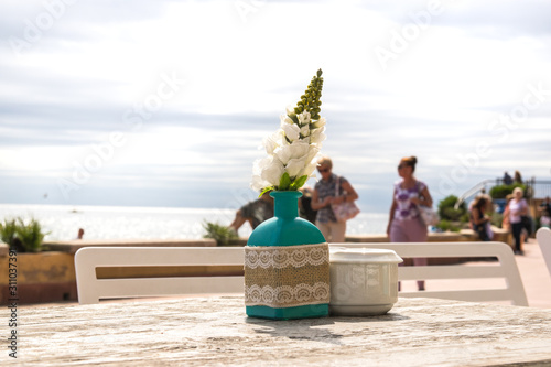 Vase with the flowers on the table with people in summer cafe. photo