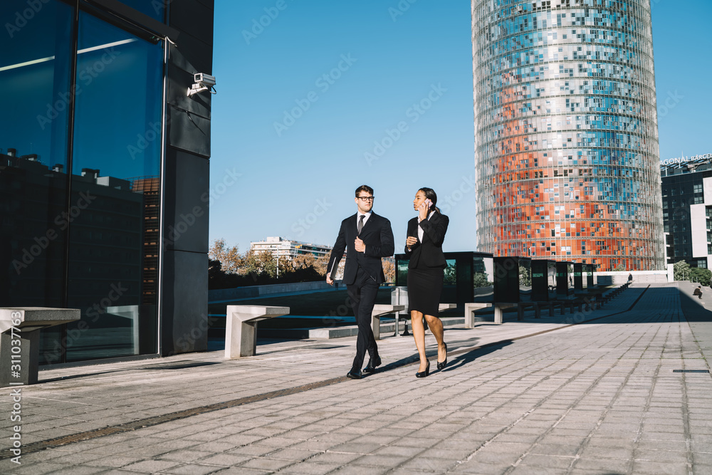 Elegant business people in modern city Young confident man walking down street with elegant black businesswoman speaking on mobile phone against shiny modern skyscraper in cityscape