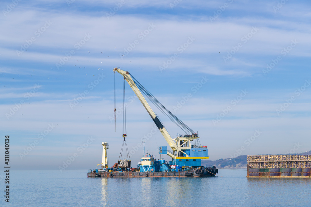 floating crane on a barge near the shore. Construction work in the sea. Construction of engineering structures on the water 