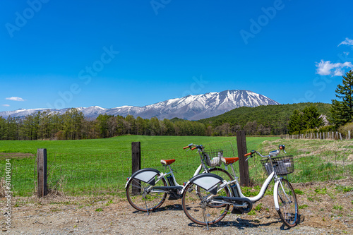 Two bicycles and forest and grass in foreground, snowcapped mountain range in background with clear blue sky in springtime season sunny day, beauty nature view, rural natural landscape