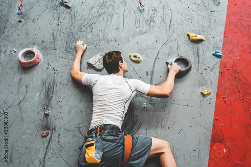 Photo Sportsman climber moving up on steep rock, climbing on artificial wall indoors