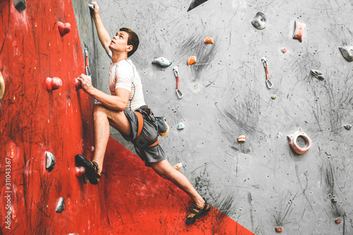 Fotografiet Sportsman climber moving up on steep rock, climbing on artificial wall indoors