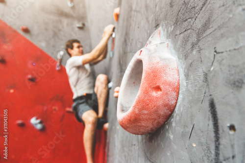Sportsman climber moving up on steep rock, climbing on artificial wall indoors. Extreme sports and bouldering concept