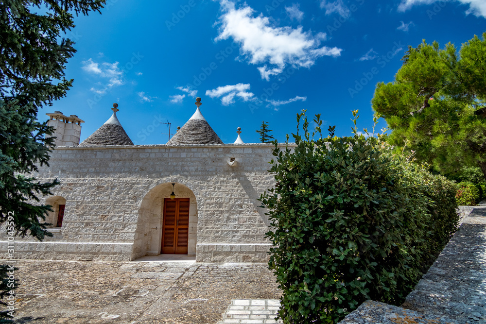 Roofs and entrance of truli, typical whitewashed cylindrical houses in Alberobello, Puglia, Italy with amazing blue sky with clouds, street view