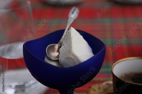 A teaspoon in a blue ice cream cup on the table, a glass of water and a cup of coffee