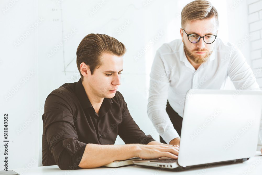 Two Young businessmen working in the office at the laptop Two Young businessmen working in the office at the laptop
