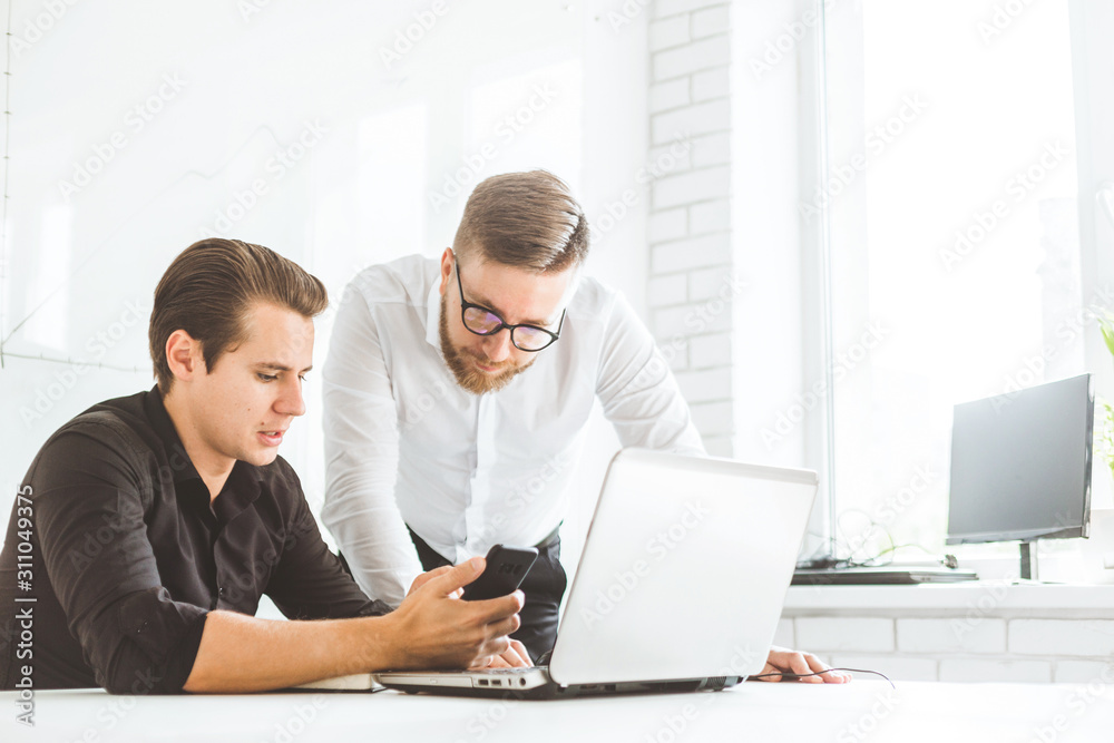 Two Young businessmen working in the office at the laptop Two Young businessmen working in the office at the laptop