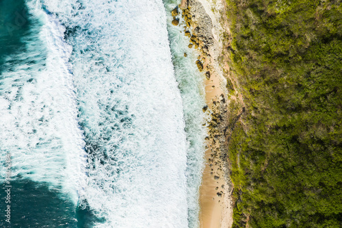 View from above, stunning aerial view of a rocky shore with a beautiful beach bathed by a rough sea during sunset, Nyang Nyang Beach (Pantai Nyang Nyang), South Bali, Indonesia.