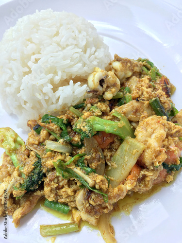 Stir fry mixed-seafood with with yellow curry powderin thai style with fried egg and rice in in white plate on white background. photo