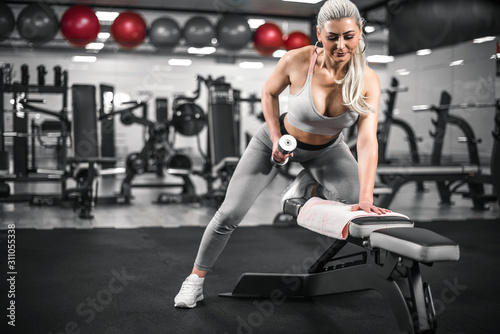 Woman doing one arm dumbell row in modern empty gym.
