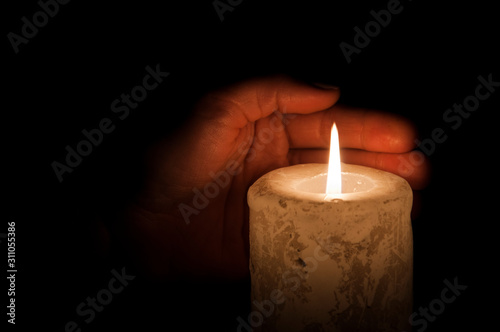 A large candle burns in the hands in the dark. On a wooden background.