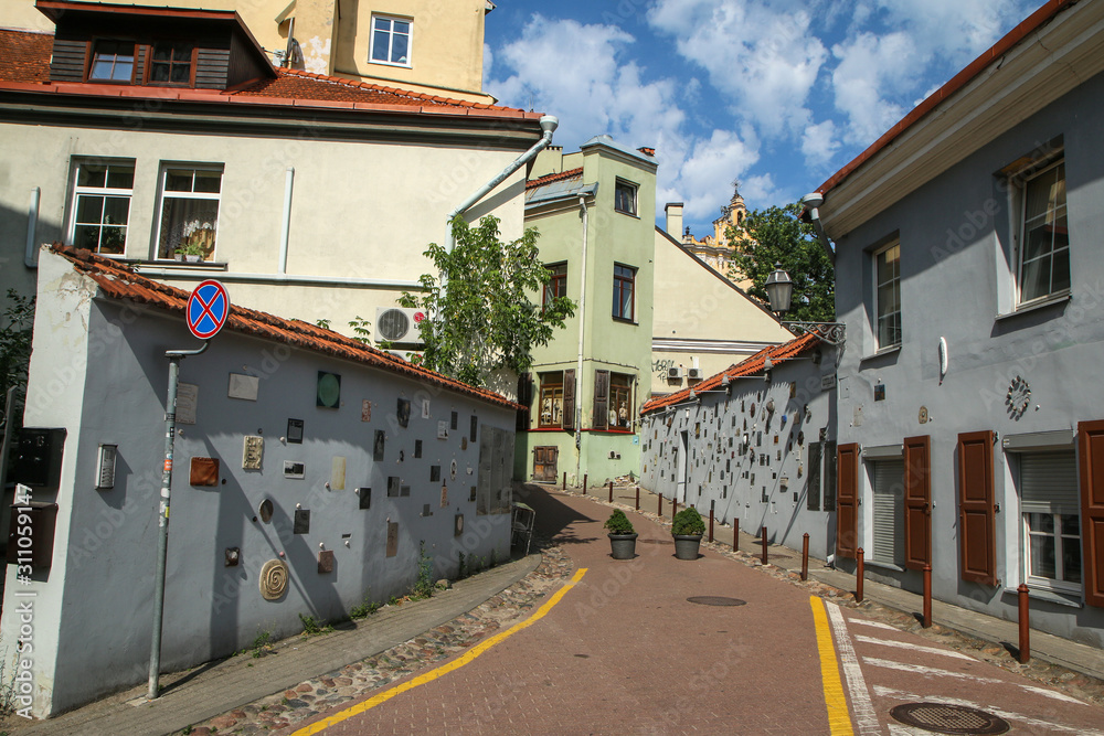 Fototapeta premium The small narrow street in Vilnius with some small artificial objects on the walls. 