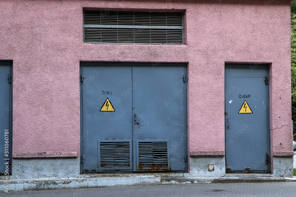 The detail of the small transformer station with metal door and warning signs on them. 