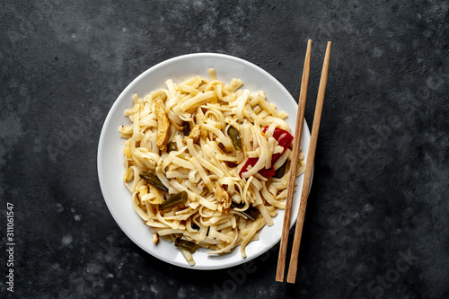 Asian food udon noodles with chicken and vegetables on a white plate on a stone background