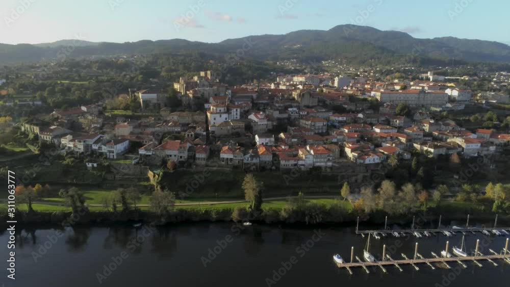 Aerial Lanscape of Tui, Galicia Spain. Panoramic view from left to right of the old city above the River Miño. Some boats moored at the docks on the river. 4k drone footage.