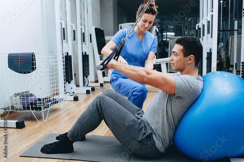 kinesiologist helps a mixed race man doing exercises to strengthen his back muscles. treatment of back pain using kinesitherapy.