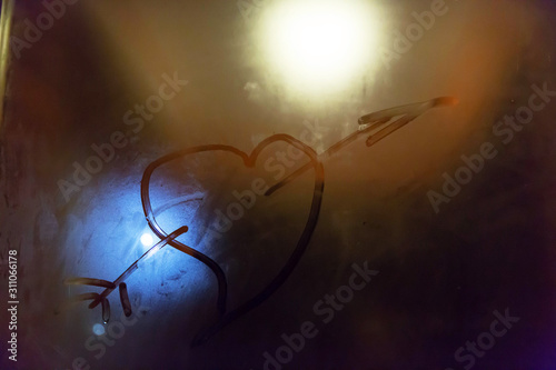 The symbol of the heart of the Cupid pierced by an arrow painted on the misted glass with a blue and yellow spot of light in the background.