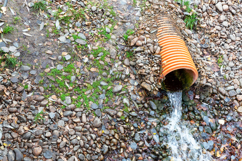 A stream of rainwater pours from an orange, plastic, sewer pipe.