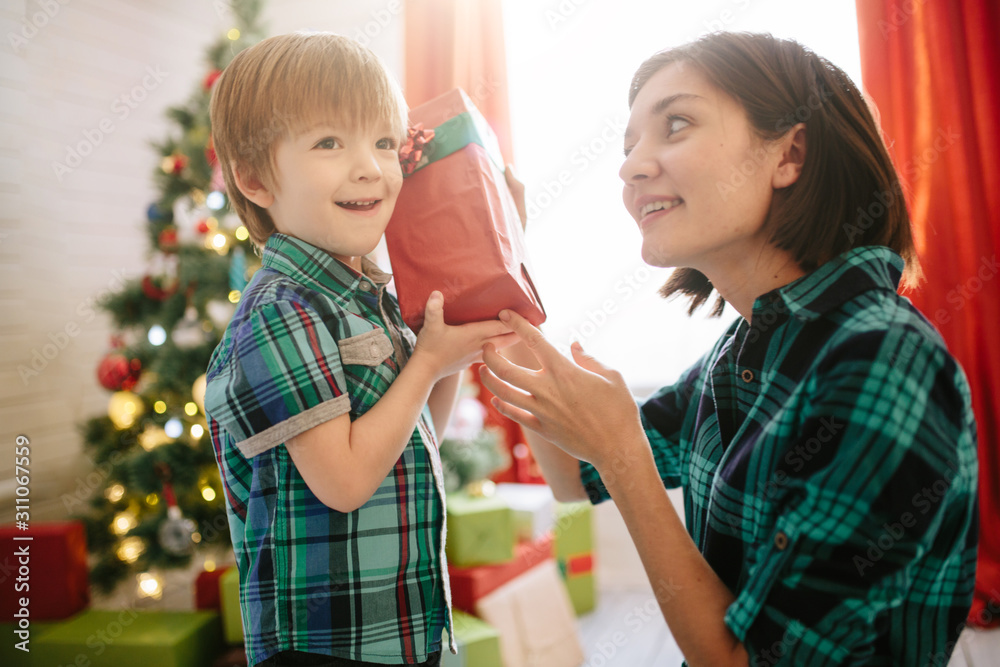 Happy family mom and son on a Christmas winter sunny morning in a decorated Christmas celebration room with a Xmas tree and gifts. Happy family mom and son on a Christmas winter sunny morning in a decorated Christmas celebration room with a Xmas tree and gifts.