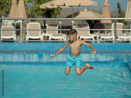 Caucasian boy in blue swimming shorts jumping into swimming at resort in summer during his summer holidays.