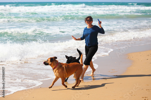 Mature Woman playing with her dogs on the beach.