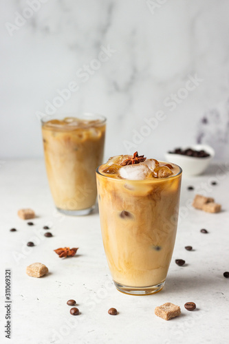 Cold brew coffee with spices and milk on light grey background. Spicy coffee with ice cubes.