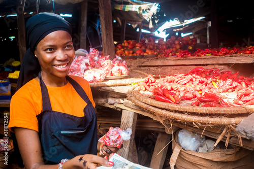 young african woman selling tomatoes in a local african market collecting money from a paying customer