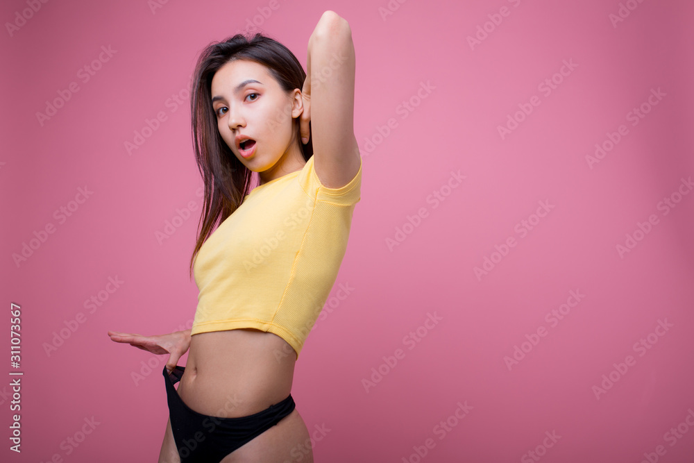 Beautiful Asian woman posing and showing how thin she pulls black panties  in f yellow t-shirt on a pink background Stock Photo