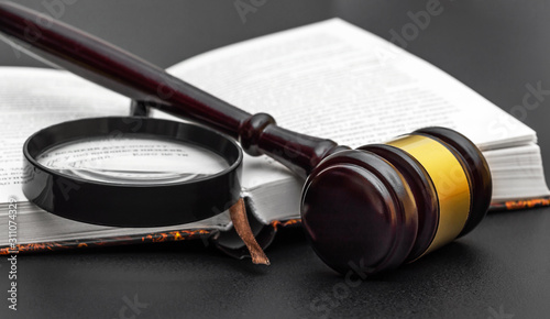 Judge's gavel with magnifying glass and book on black. Juristic concept. photo