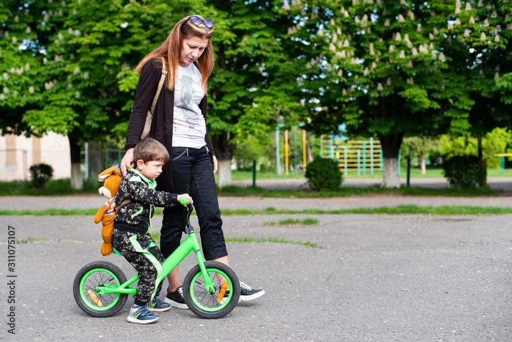 Woman spends time with her little son, mom supports her son so he doesn't fall off the bike because he just learned to ride Woman spends time with her little son, mom supports her son so he doesn't fall off the bike because he just learned to ride