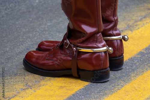 Male adult shinny brown leather boots with a buckle and spur. The person is standing on a bright yellow painted line on the road. © Dolores  Harvey