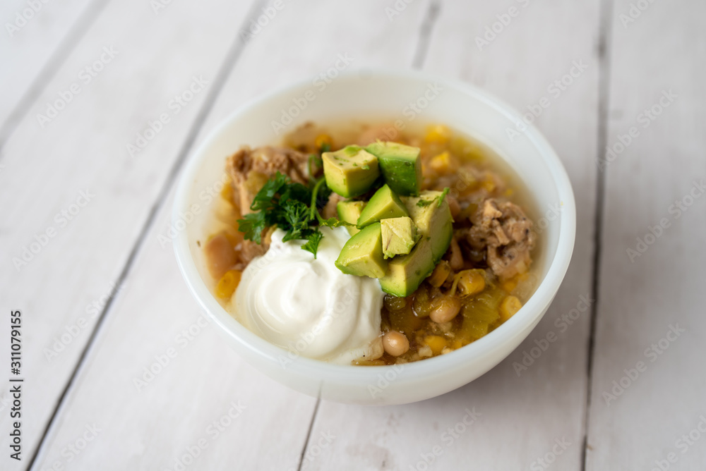 Flavorful White Chicken Chili made with hearty beans, tender chicken, and a rich and creamy broth in slow cooker, garnished with sour cream and avacado