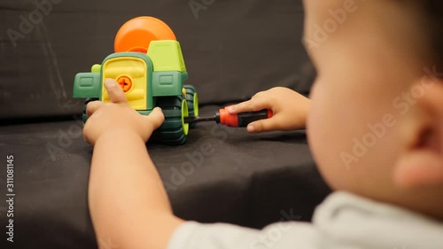 Little kid play with plastic car. Repairing a toy concrete mixer with screwdiver photo