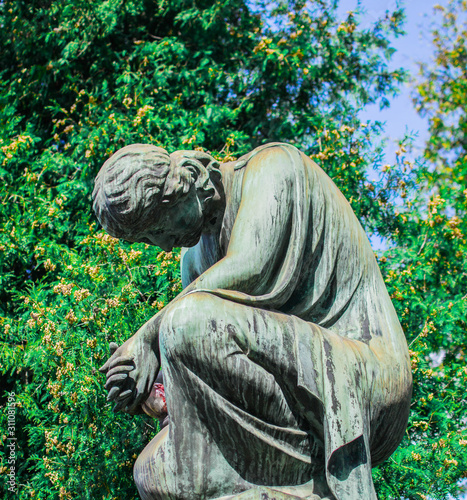 Stone statue of a grieving and praying woman in a park.