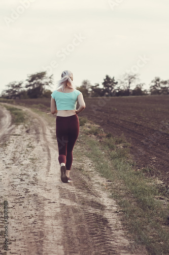 back of young woman in sportswear running distance in the field, girl engaged in sport outdoors on a cloudy day, concept healthy lifestyle and bodycare