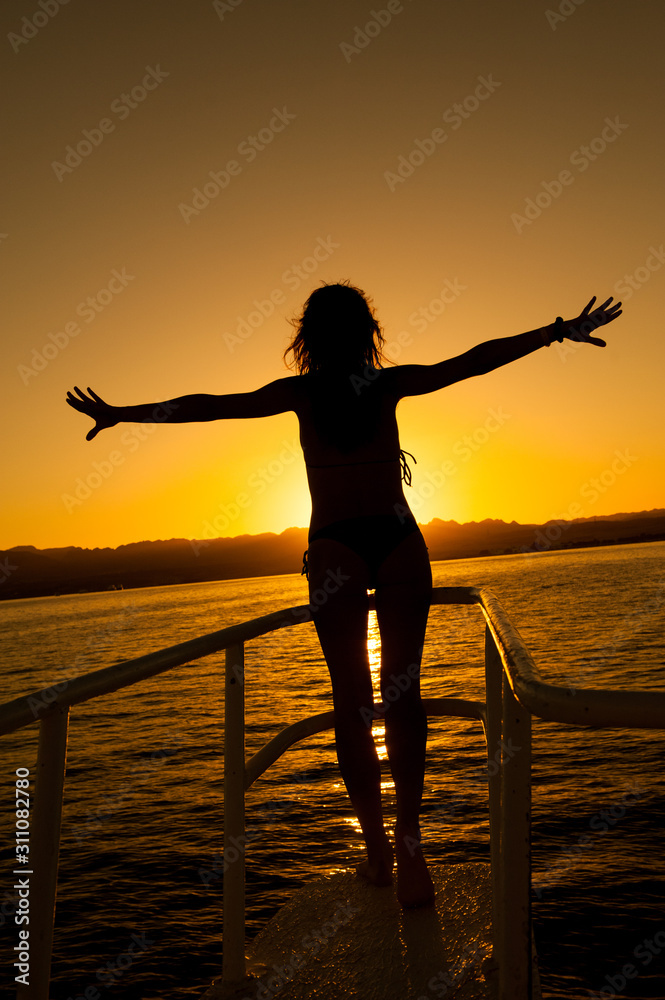 Fototapeta premium Woman silhouette posing against the sun on a sunset in the sea